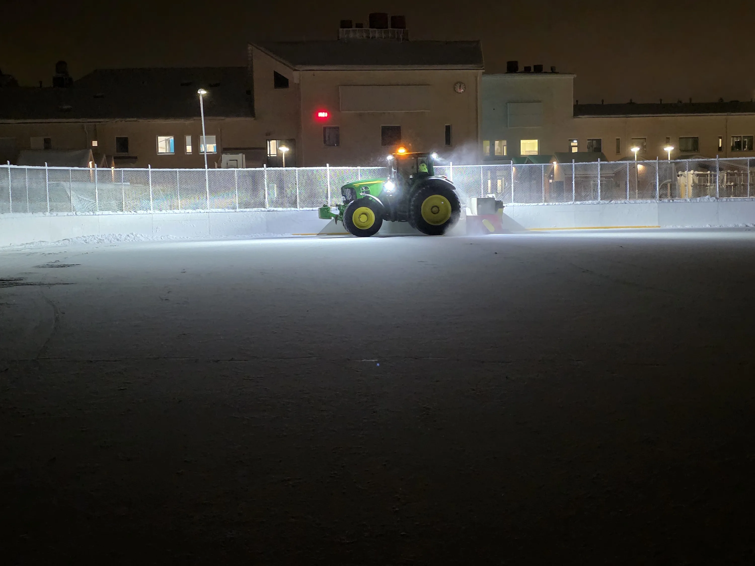Jääkenttää auraava traktori yöllä, valaistus korostaa lunta.